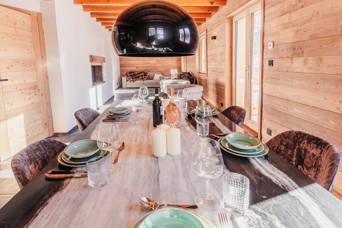 A dining area with a long table set for six, wooden walls, and a large arched ceiling.