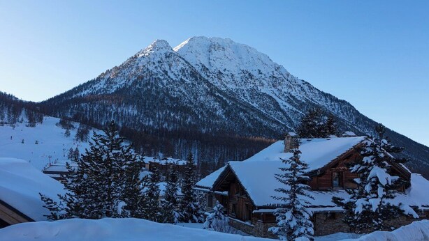 Una montagna innevata con una baita di legno in primo piano.