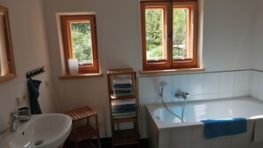 Bathroom features a large bathtub, sink, and two windows with a wooden shelf for towels.