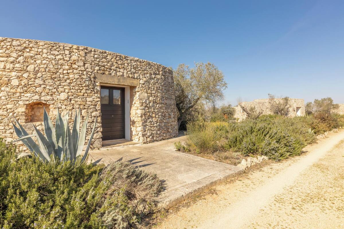 A stone building with a door and window, surrounded by vegetation and a dirt path.