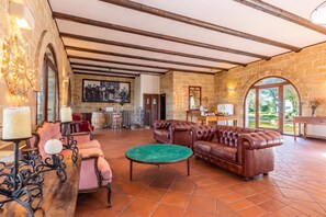 A spacious living area with a stone wall, a fireplace, a large leather sofa, and a dining area with a table and chairs. - Villetta Il Morige (Galatone)
