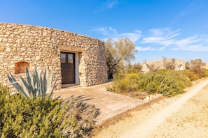 A stone building with a door and window, surrounded by vegetation and a dirt path. - Villetta Il Morige (Galatone)