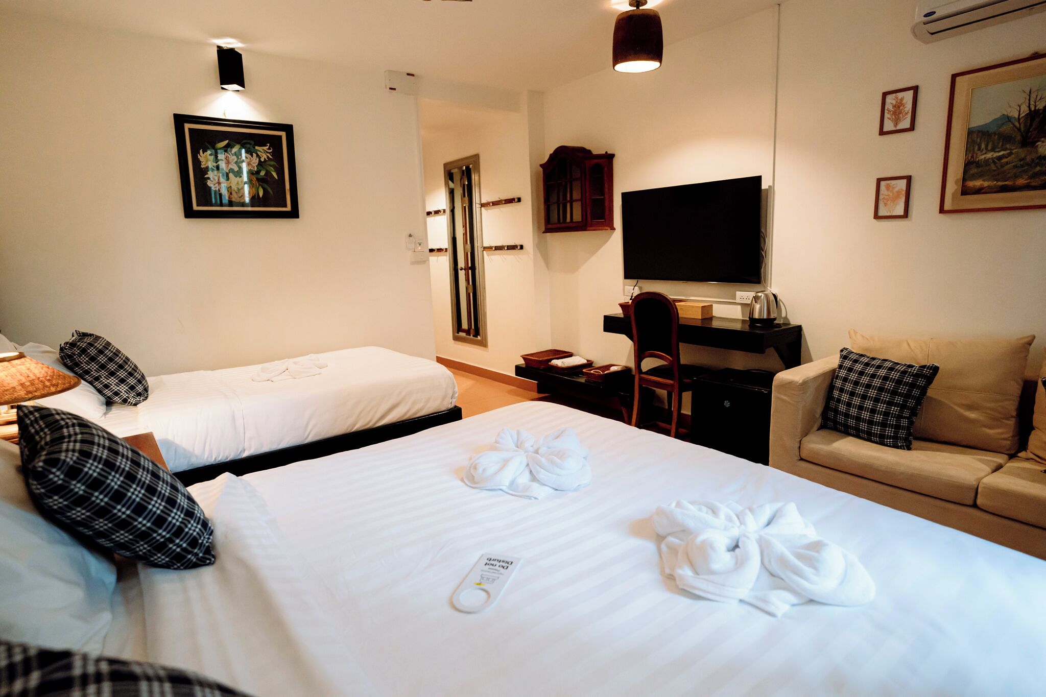 A hotel room with two beds, a desk, a chair, a TV, and a couch.