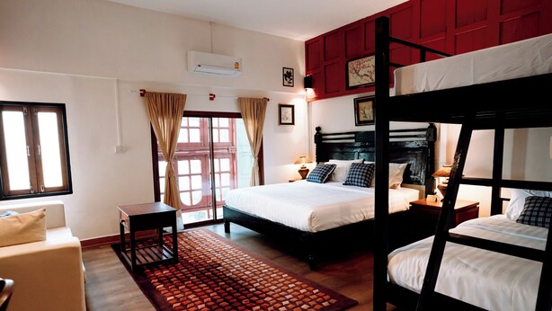 A hotel room with a bunk bed, a sofa, a small table, and a window with curtains.