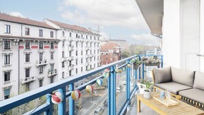 A balcony with a sofa and a table, overlooking a street with buildings. - Easylife - Cozy two-level unit in Isola (Milano)
