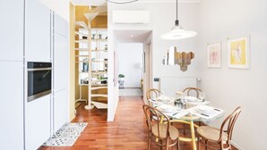 A modern kitchen with white cabinets, a built-in oven, and a dining area with a glass table and wicker chairs. - Easylife - Cozy two-level unit in Isola (Milano)