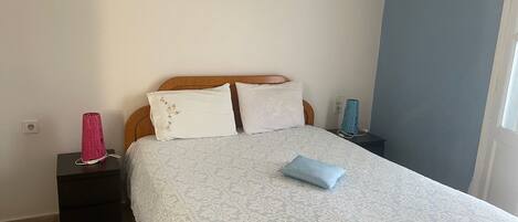 A bedroom with a bed, two pillows, a bedside table with a lamp, and a wall-mounted picture.