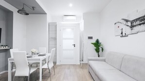 Un salon moderne avec un canapé blanc, une table à manger avec des chaises et un coin cuisine équipé de placards et d’un réfrigérateur.