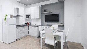 Une cuisine moderne avec des meubles blancs, un four à micro-ondes encastré et un coin repas comprenant une table et des chaises blanches.