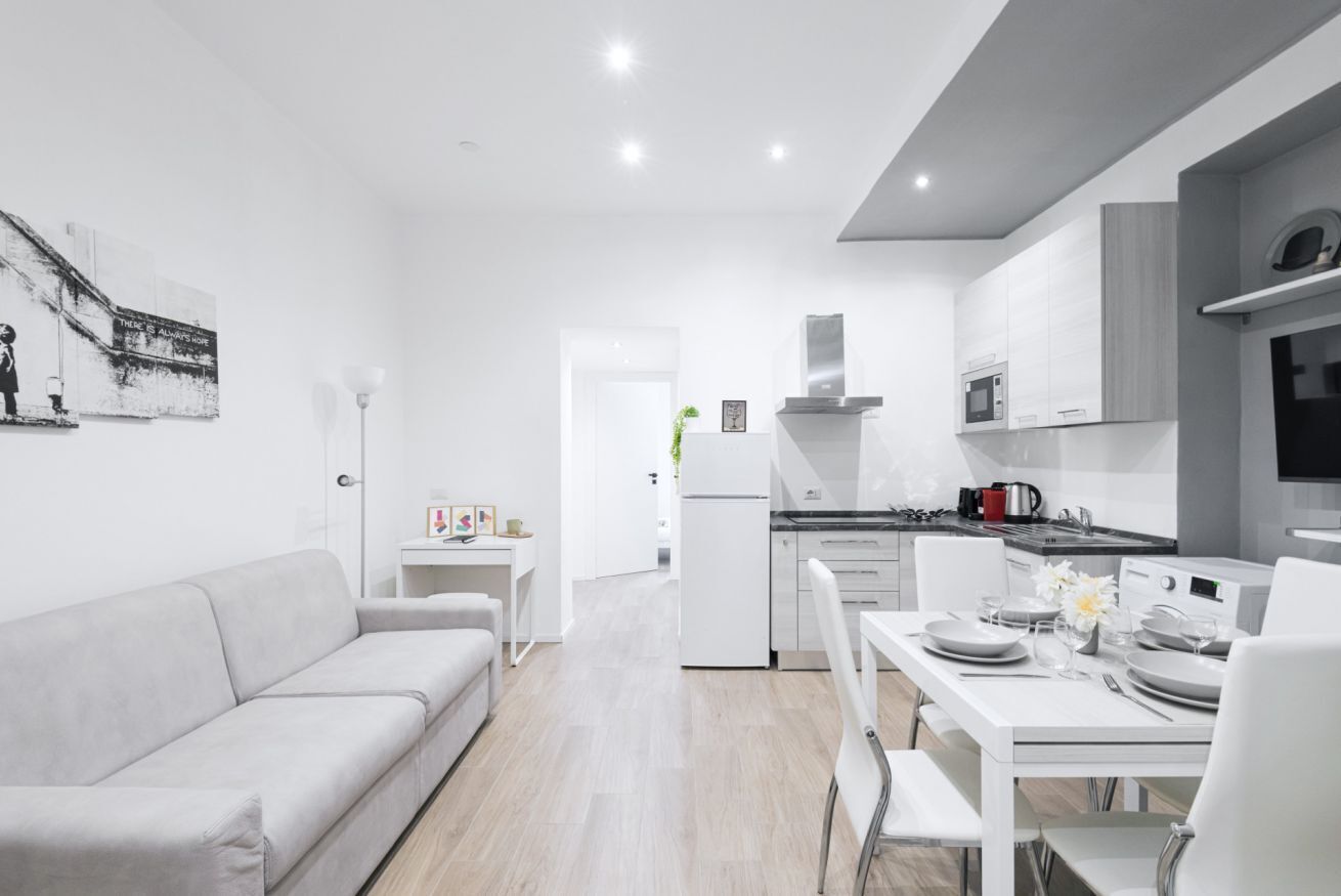 Een moderne keuken met witte kasten, een eettafel voor vier personen en een bank in de woonkamer.