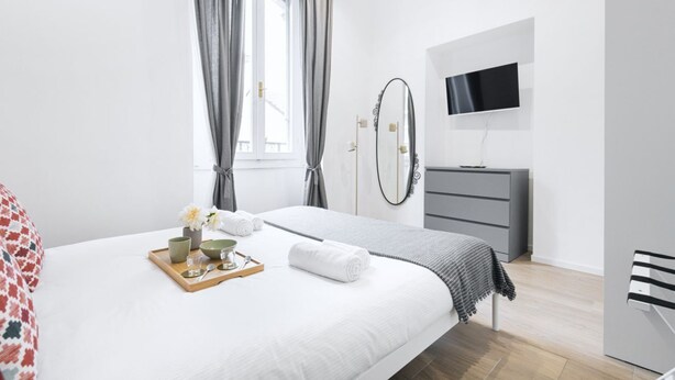 Une chambre à coucher moderne, équipée d’un lit, d’une télévision, d’une commode et d’une fenêtre avec des rideaux.