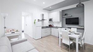 Une cuisine moderne avec des meubles blancs, un coin repas avec des chaises blanches et un téléviseur à écran plat fixé au mur.