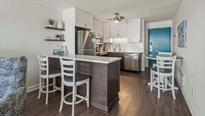 Cozinha moderna com armários brancos, uma ilha central com banquetas, uma geladeira e uma porta azul.