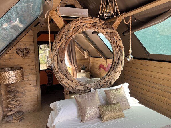 Une chambre confortable avec un lit suspendu en forme d’anneau en bois, un grand miroir et une vue sur l’extérieur.