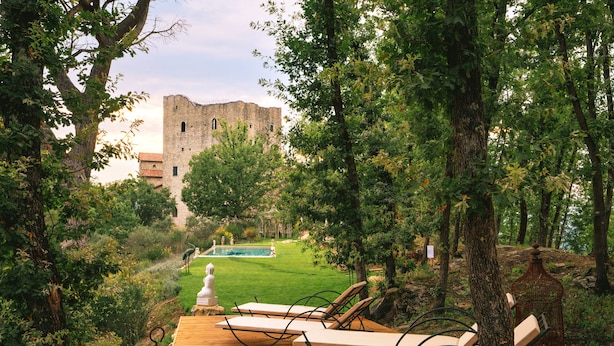 A wooden deck with lounge chairs overlooking a lush garden and a historic building in the background. - tenuta castel dell'aquila (Fivizzano)