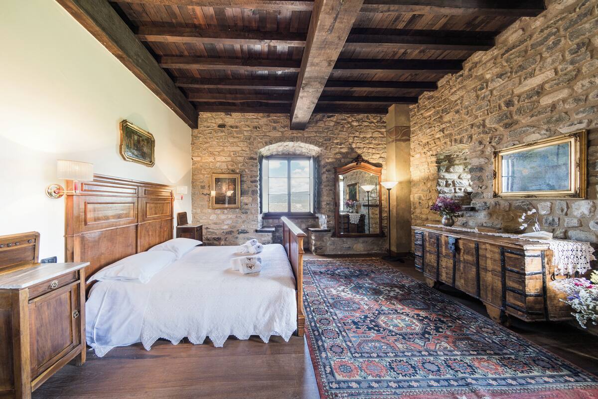 A rustic bedroom with a wooden bed, stone walls, and a large rug.