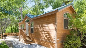 A wooden cabin with a porch, a staircase, and a view of the surrounding forest. - Overlook Cabin at KRS Camp James (Cabin 3) (Kernville)