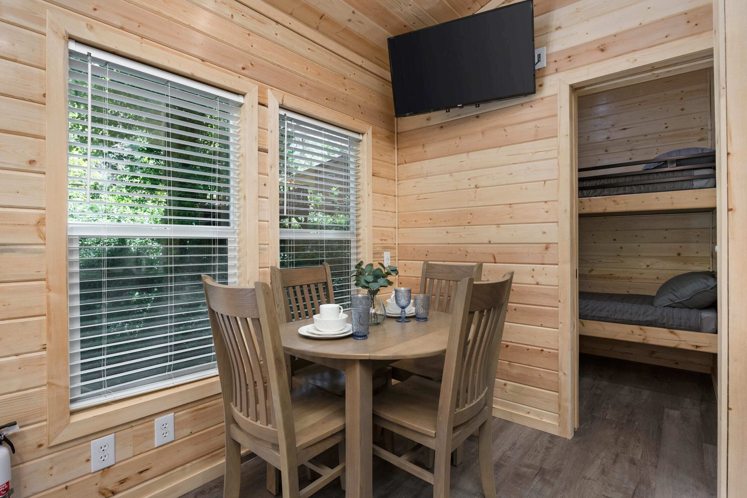 Una cabaña de madera con una mesa de comedor, sillas, un televisor montado en la pared y una litera.