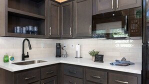 A modern kitchen with dark cabinets, a stainless steel sink, a black faucet, a coffee maker, and a microwave. - Overlook Cabin at KRS Camp James (Cabin 3) (Kernville)