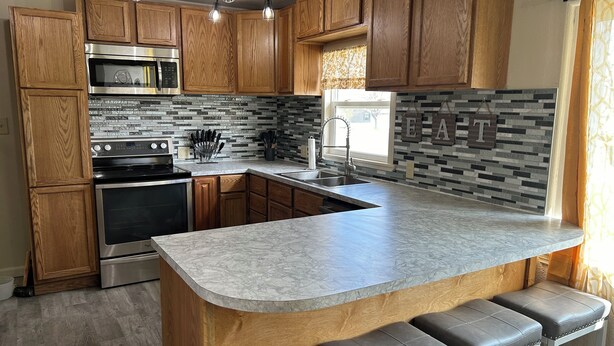 A modern kitchen with wooden cabinets, a stainless steel oven, a built-in microwave, a granite countertop, and a bar area with stools. - A newly renovated home full of fun games for the entire family to enjoy. (Thermopolis)