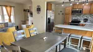 A modern kitchen with a stainless steel refrigerator, a microwave, and a built-in oven. There is a dining area with a wooden table and chairs, and a kitchen island with stools. - A newly renovated home full of fun games for the entire family to enjoy. (Thermopolis)