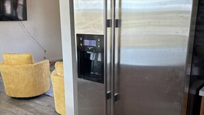 A stainless steel refrigerator with a water dispenser, a flat-screen TV mounted on the wall, and a yellow armchair in a kitchen area. - A newly renovated home full of fun games for the entire family to enjoy. (Thermopolis)