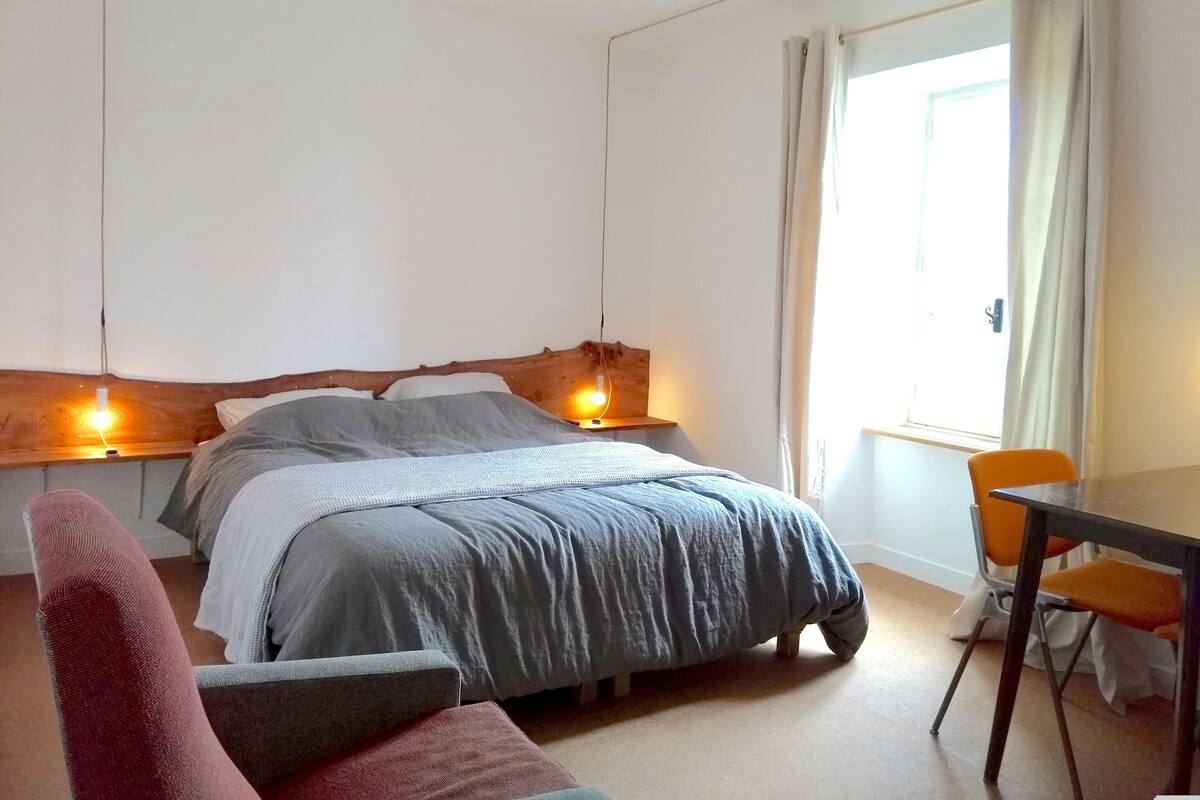 Ein Schlafzimmer mit einem Bett, Nachttischlampen, einem Sessel und einem Tisch.