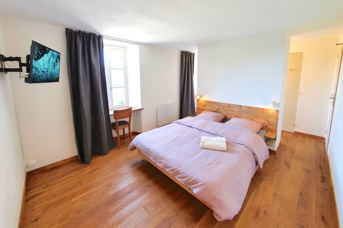 Ein Schlafzimmer mit Holzboden, einem Bett mit Kopfteil, einem Schreibtisch mit Stuhl und einem Fenster mit Vorhängen.
