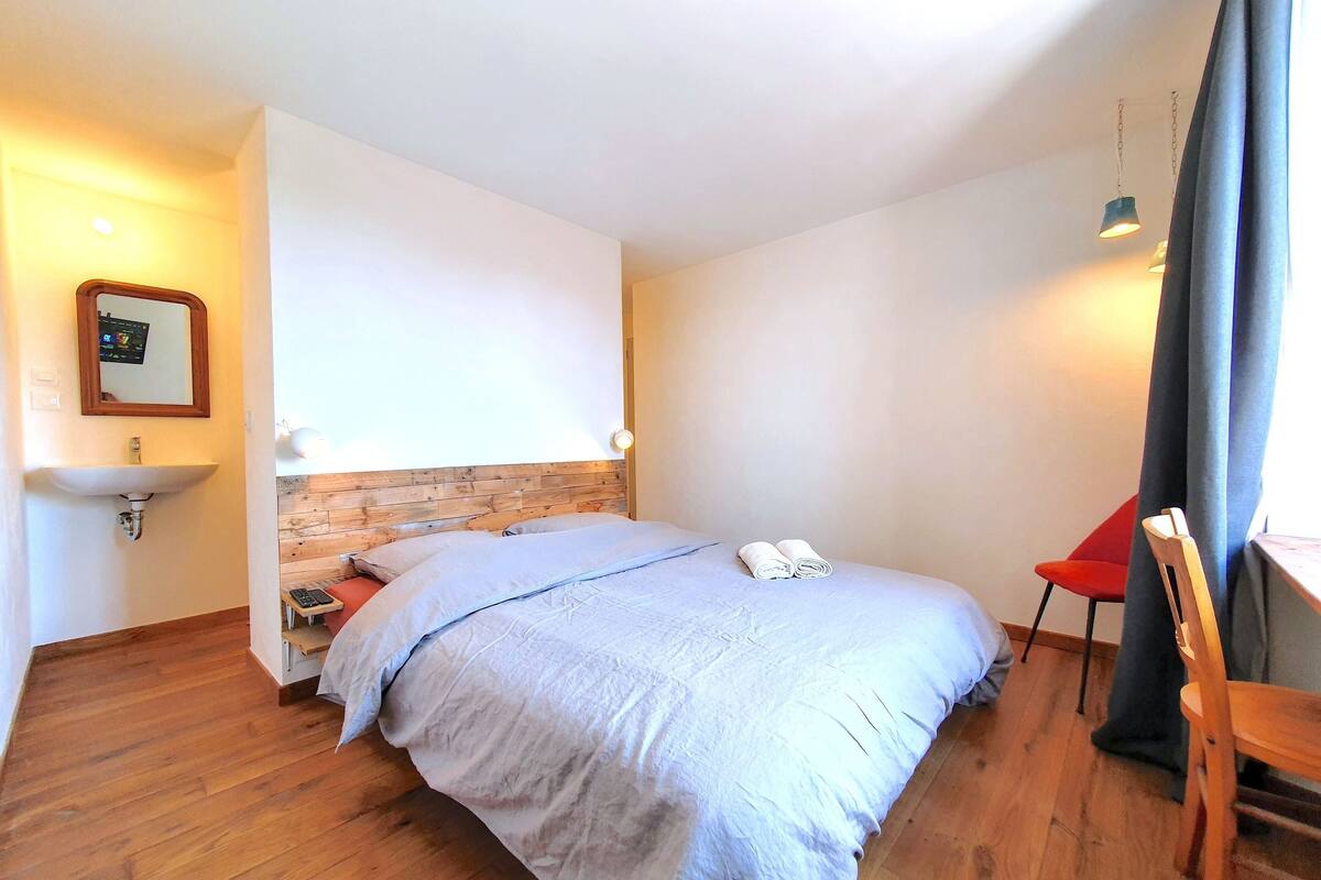 Ein Schlafzimmer mit hölzernem Kopfteil, einem Bett mit blauer Bettdecke, einem roten Sessel und einem Holztisch.