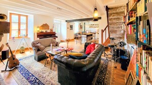 Un salon chaleureux avec un piano, un canapé, une bibliothèque et, au fond, un coin repas.
