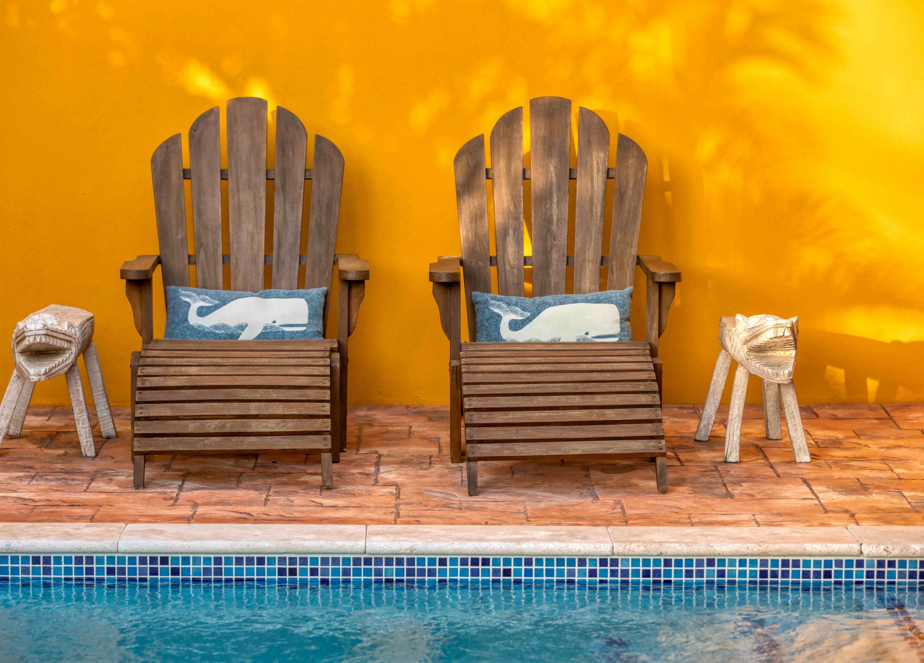 Zwei Adirondack-Stühle mit Walmotiven auf den Kissen an einem Pool mit einer gelben Wand.