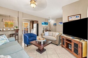 A living room with a sofa, a blue armchair, a coffee table, a television, and a cabinet with a TV stand.