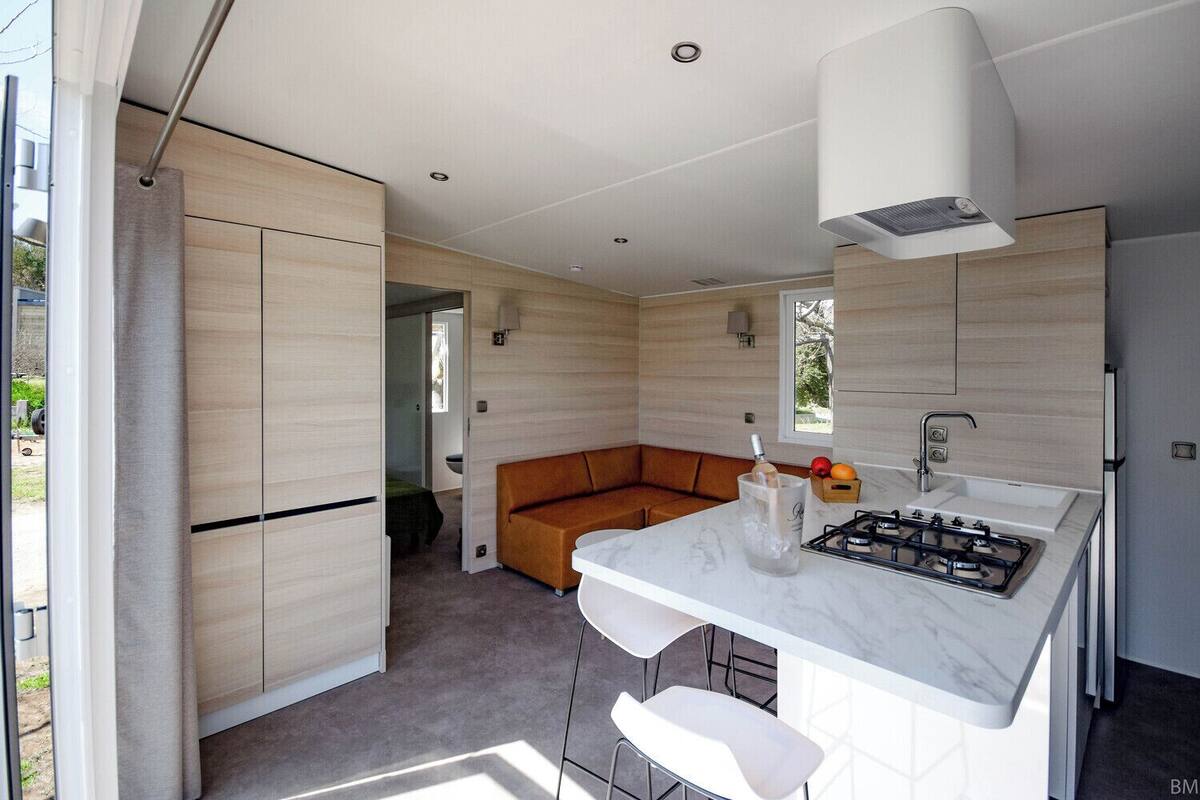 Een moderne keuken met een gasfornuis, een spoelbak en een inbouwoven. Er staat een houten bankje in de hoek en een raam zorgt voor natuurlijk licht.