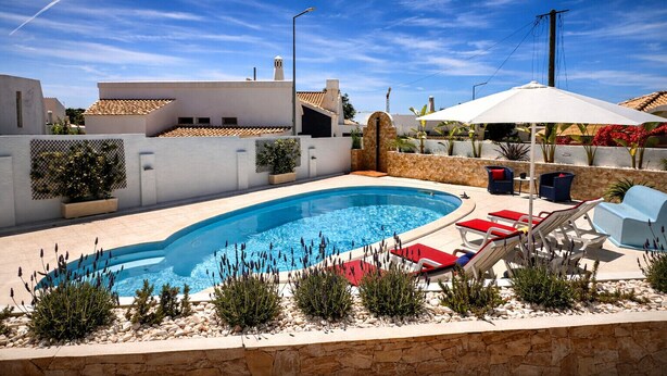 A swimming pool with lounge chairs and umbrellas, surrounded by a stone wall and plants.