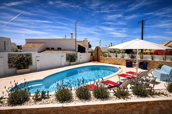 A swimming pool with lounge chairs and umbrellas, surrounded by a stone wall and plants.