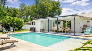 Ein Schwimmbecken mit Liegestühlen, eine überdachte Terrasse mit Tisch und Stühlen sowie ein Grill.