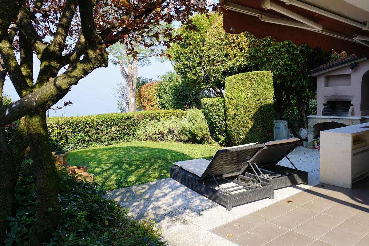 Une terrasse extérieure équipée d’un barbecue, de sièges et offrant une vue sur le jardin.