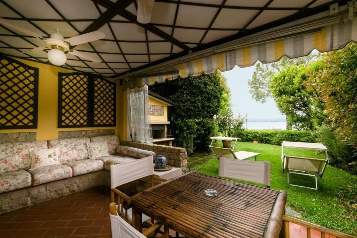 Un patio couvert comprenant une table en bois, des chaises blanches, un canapé à motifs floraux et un ventilateur de plafond.