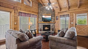 Een knus interieur van een chalet met een stenen openhaard, houten wanden en een plafondventilator.