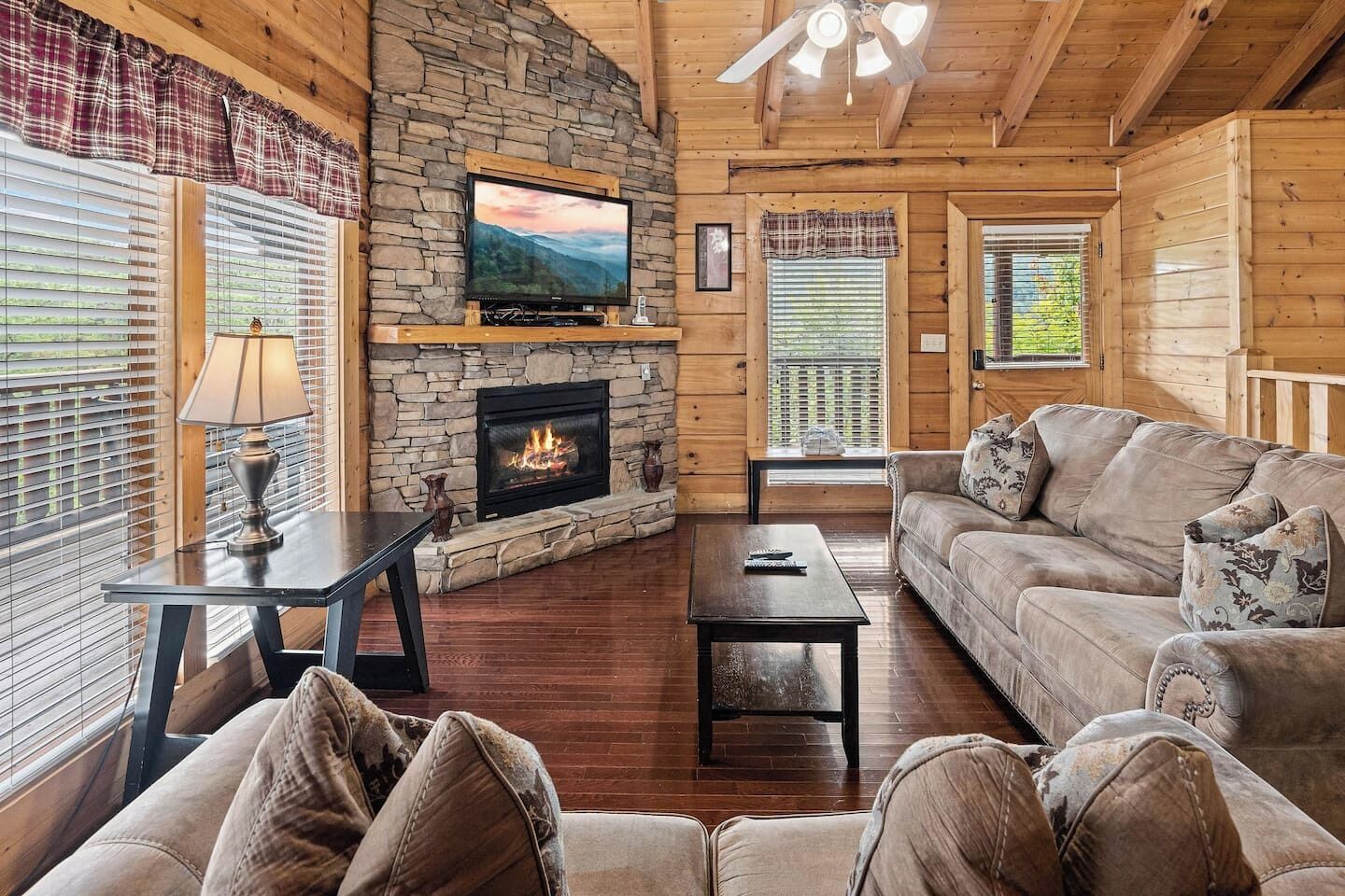 A cozy cabin interior with a stone fireplace, a television mounted above it, a sofa, and a coffee table.