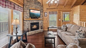 Een gezellig cabin interieur met een stenen open haard, een televisie erboven, een bank en een bijzettafeltje.