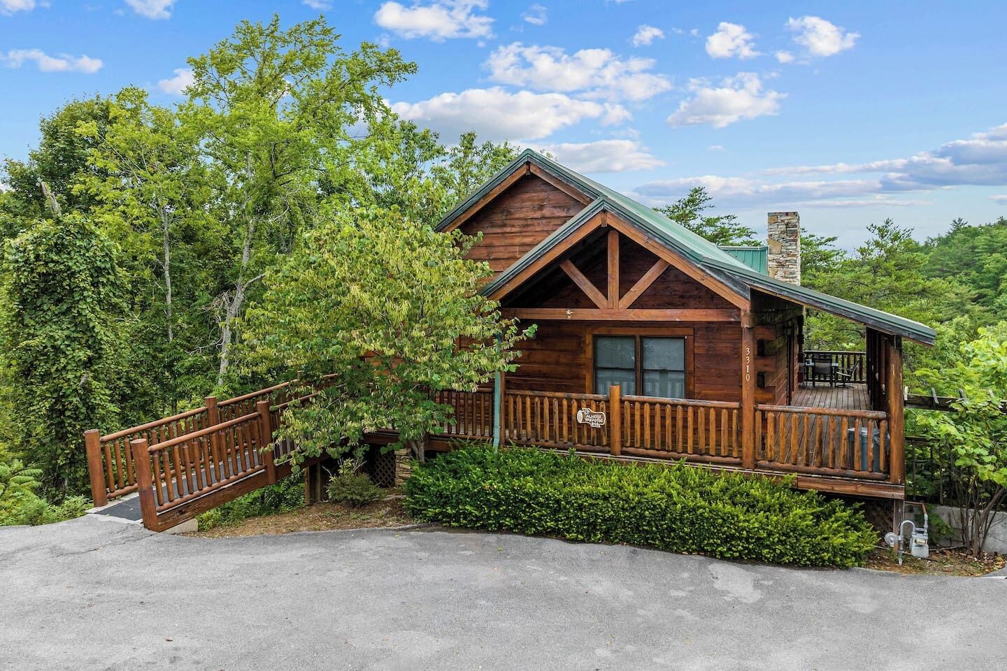 A wooden cabin with a balcony, surrounded by lush greenery.