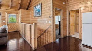 Een houten chaletinterieur met een trap, een lijst met foto aan de muur, en een witte koelkast.