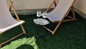 Una terraza con dos sillones de descanso y una pequeña mesa con dos vasos de agua.
