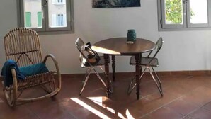 Una habitación con una mesa redonda, dos sillas, un sillón de mimbre y un cuadro en la pared.