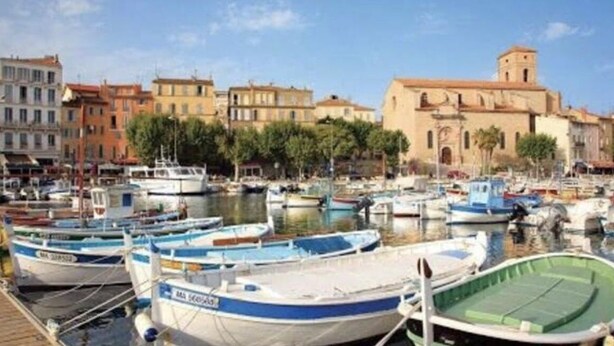 Un puerto deportivo con varios barcos amarrados, un edificio frente al agua y un cielo despejado.