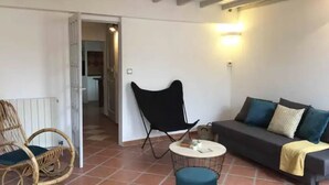 Una sala de estar con un sofá, una silla negra, un sillón de mimbre y una pequeña mesa redonda.