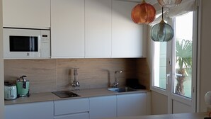A modern kitchen with white cabinetry, a microwave, a sink, and a window with a view of palm trees. - El Capricho Suite La Terraza con Parking Incluido (Gijón)