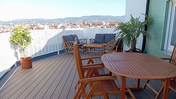 A wooden deck with outdoor furniture, including a table and chairs, and a potted plant. - El Capricho Suite La Terraza con Parking Incluido (Gijón)