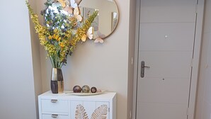 A room with a white cabinet, a round table with a woven seat, a mirror, and a vase with flowers. - El Capricho Suite La Terraza con Parking Incluido (Gijón)